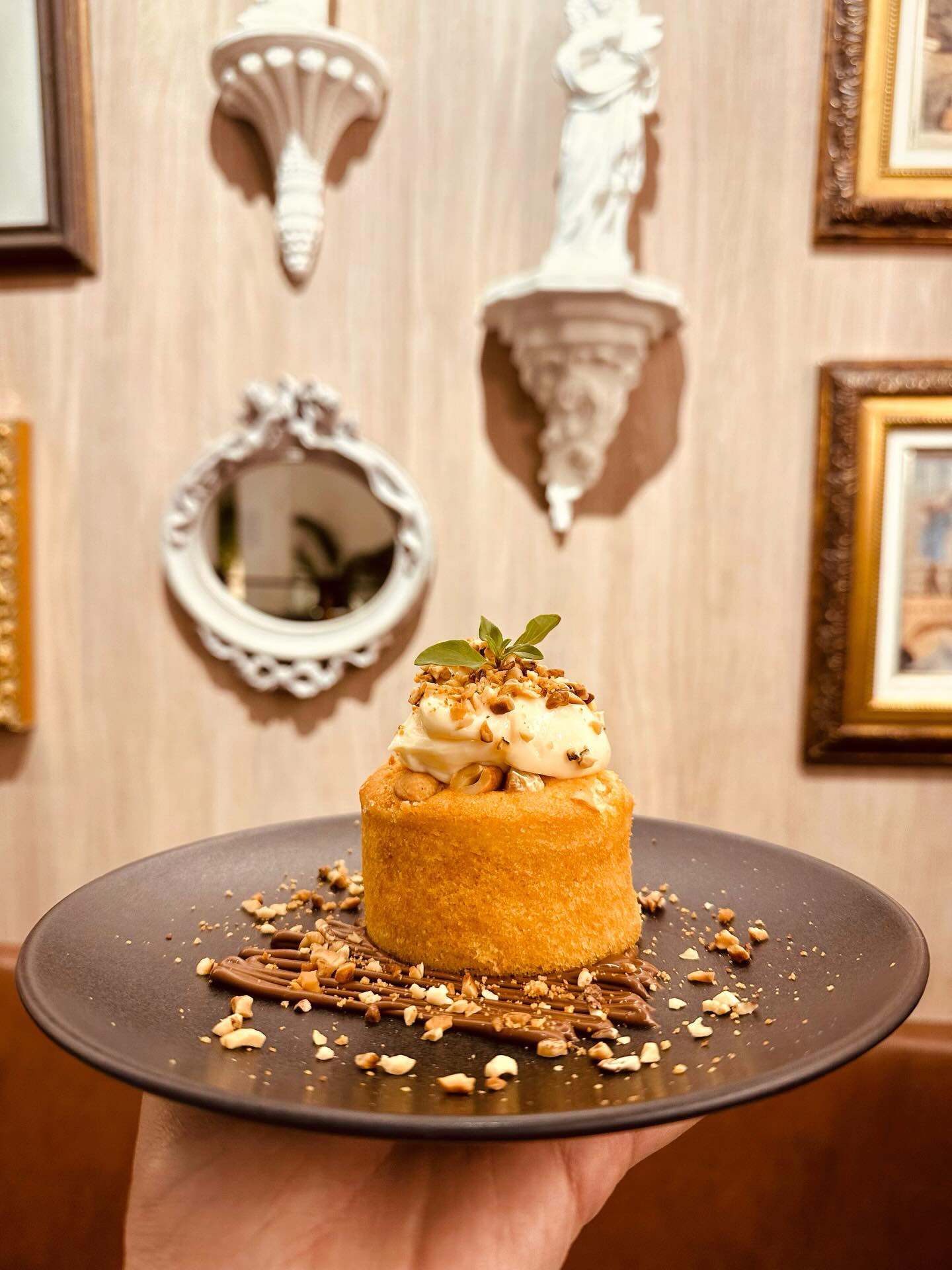 Prato com bolinho e creme diante da parede com espelho, quadros e esculturas
