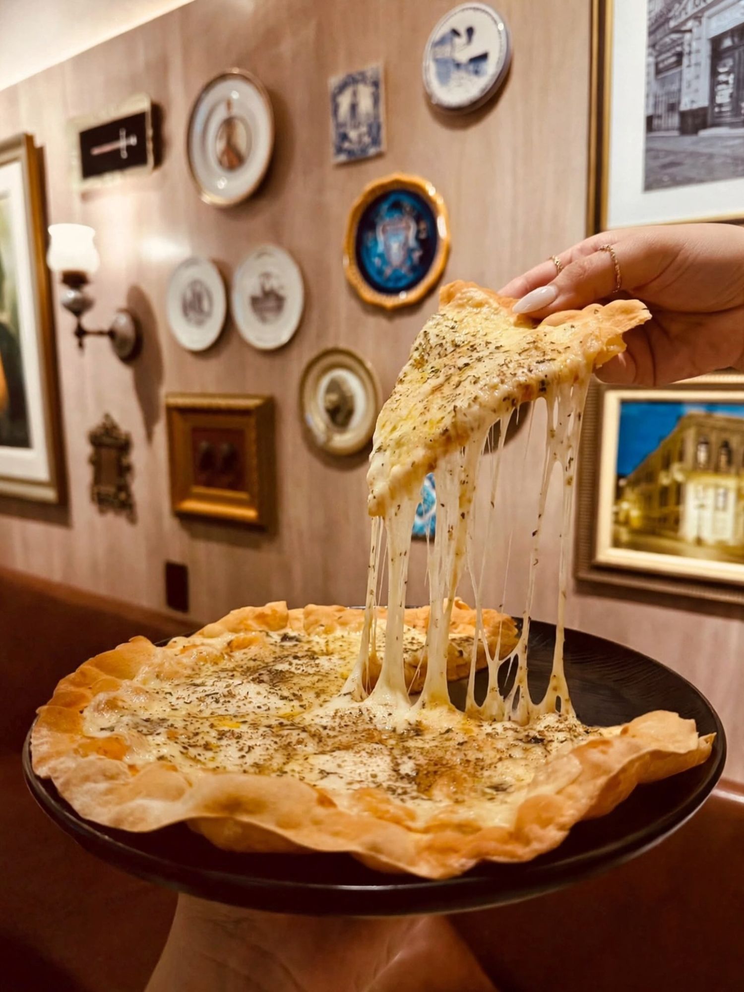 Fatia de pizza individual com queijo derretido puxando, em frente à parede de pratos decorativos